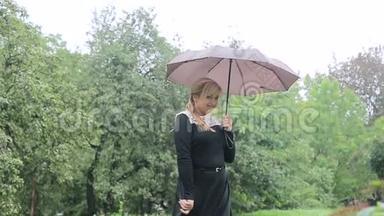 雨中带着雨伞的女人向<strong>公园</strong>里的照相机摆姿势。 穿着黑色礼服带伞的女孩